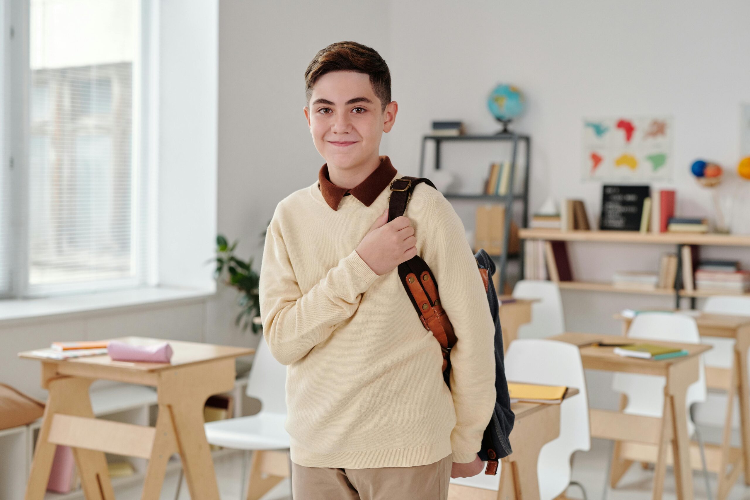 Male student smiling as he wears a backpack and stands in a classroom.