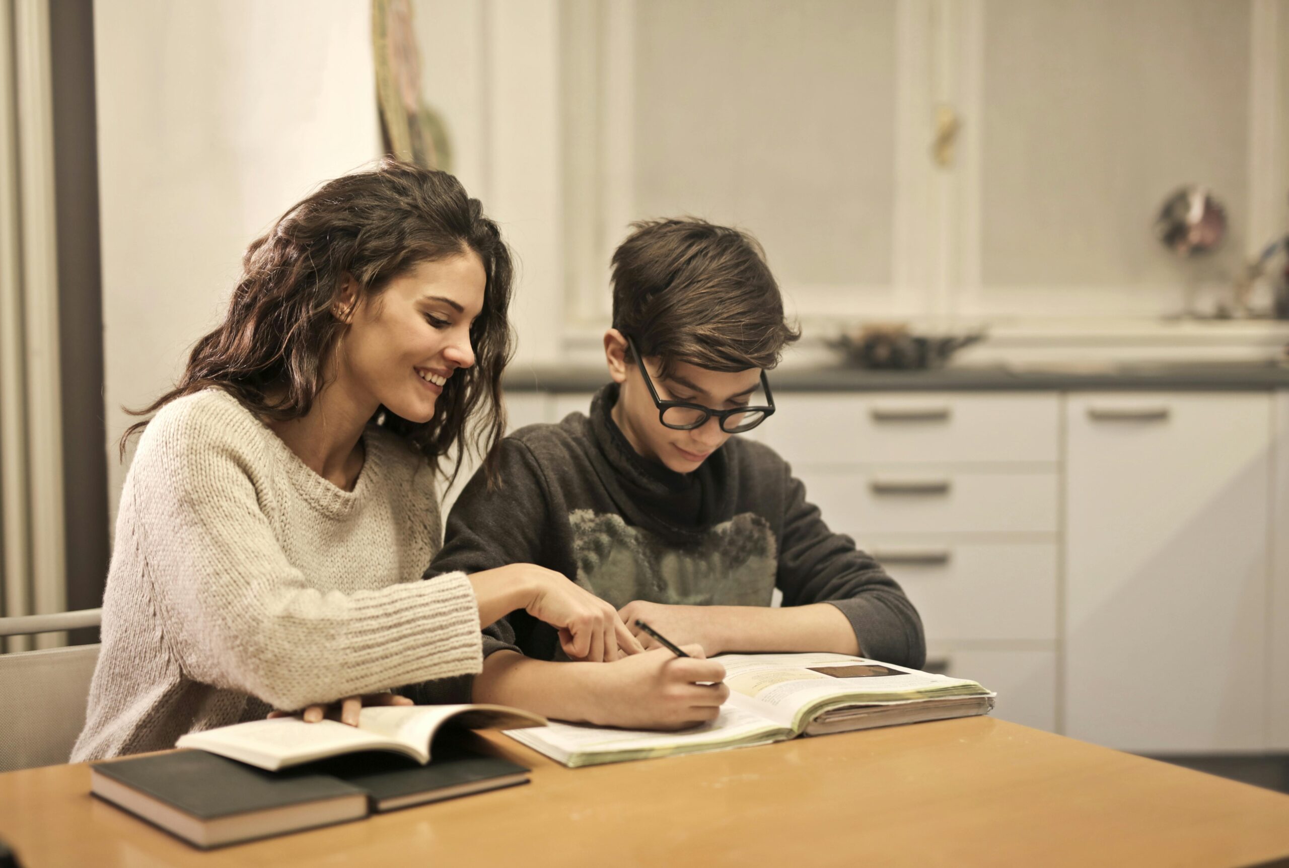 Female educator instructing a male student as he writes in a workbook.